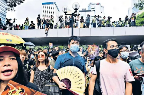  ??  ?? Defiant pro-democracy protesters march through Hong Kong yesterday and, below, demonstrat­ors hold umbrellas to shield themselves from tear gas during clashes with police