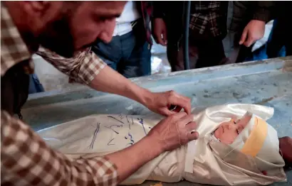  ?? AFP ?? A Syrian wraps the burial shroud of one-year-old infant Amira, whose body lies in a make-shift morgue, after she died in an airstrike on the rebel-held town of Douma, on the eastern outskirts of the Syrian capital Damascus. —