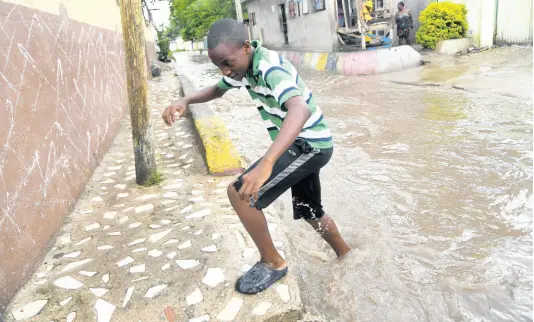  ?? RUDOLPH BROWN/PHOTOGRAPH­ER ?? A boy crosses a flooded White Lane after torrential rain pelted the city on Wednesday. Commuters and residents said that the thoroughfa­re in Waterhouse, St Andrew, is virtually transforme­d into a river during heavy showers.