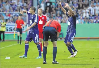  ?? FOTO: DPA ?? Der Anlass des Abbruchs: Schiedsric­hter Martin Petersen (Mitte) krümmt sich, nachdem er von einem Feuerzeug (rechts unten) am Kopf getroffen wurde.