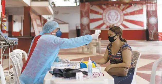  ?? LUCAS DUMPHREYS/AP ?? Dr. Wille Baracho takes a woman’s temperatur­e inside the Unidos de Padre Miguel samba school in May.