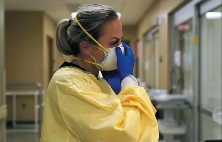  ?? JEFF ROBERSON — THE ASSOCIATED PRESS FILE ?? Registered nurse Chrissie Burkhiser puts on personal protective equipment as she prepares to treat a COVID-19 patient in the emergency room at Scotland County Hospital in Memphis, Mo., Nov. 24. U.S. hospitals slammed with COVID-19 patients are trying to lure nurses and doctors out of retirement and recruiting nursing students and new graduates who have yet to earn their licenses.