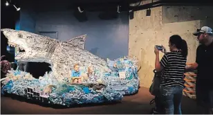  ??  ?? Children sit in part of a boat incorporat­ed into the statue of "Greta the Great White Shark," which is part of Angela Haseltine Pozzi's project "Washed Ashore: Art to Save the Sea."