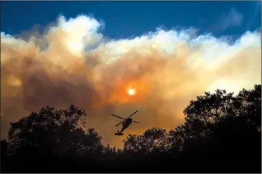  ?? AP/NOAH BERGER ?? Smoke billows from the Camp Fire as a firefighti­ng helicopter hovers Sunday near Pulga, Calif.