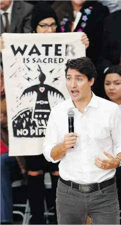  ?? JOHN WOODS / THE CANADIAN PRESS ?? Prime Minister Justin Trudeau speaks with the public as a pipeline protester using an indigenous theme stands behind him at a town-hall meeting Thursday in Winnipeg.