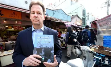  ?? AFP photo ?? File photo shows Patrick Ramage, global whale programme director of the Internatio­nal Fund for Animal Welfare (IFAW), holding a report on the economics of Japan’s whaling industry outside Tsukiji Market, Japan’s biggest fish market, in Tokyo. —