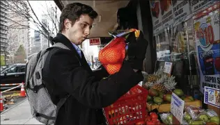  ?? ASSOCIATED PRESS ?? Yale junior Liam Elkind, 20, selects a bag of oranges at the Associated Supermarke­t for 83-year-old Carol Sterling, who is self-quarantine­d in her apartment in New York. Elkind and his friend, Simone Policano, amassed 1,300 volunteers in 72 hours to deliver groceries and medicine to those in need.