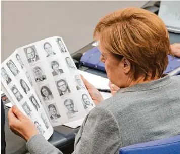  ?? Foto: Wolfgang Kumm, dpa ?? Alte und neue Gesichter im Bundestag: Auch Bundeskanz­lerin Angela Merkel verschafft sich in der Auftaktsit­zung in einer eilig ge  druckten Broschüre einen ersten Überblick.