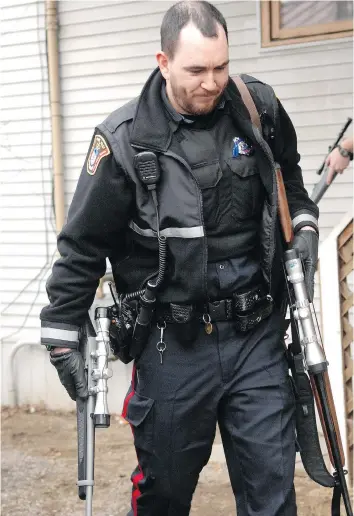  ?? DON HEALY/FILES ?? A Regina Police Service officer carries two long guns seized from a home on the 2200 block of Osler Street in March of 2010. The rifle in his right hand is comparable to the one used to kill Matthew Wells.