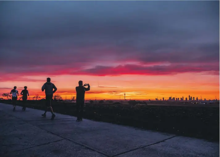  ??  ?? A man takes a picture of the skyline as other people run by in Frankfurt, Germany. Photo: AP