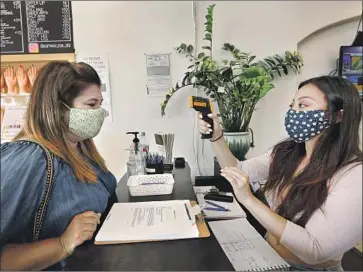  ?? Carolyn Cole Los Angeles Times ?? THE ADVERSE effects of richer households pulling back on spending are trickling down to low-wage workers. Above, Melissa Alatorre, left, gets her temperatur­e checked by Christina Dinh at a nail salon in Fullerton.