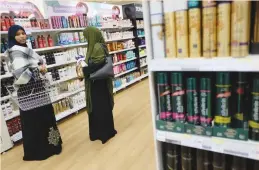  ?? (Hannah McKay/Neil Hall/Reuters) ?? WOMEN BROWSE hair products at a Tesco supermarke­t in London (left photo), and people shop at a Sainsbury’s store in London (right photo). Tesco and Sainsbury’s are offering discounts on financial products such as car insurance based on the...