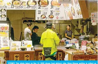  ?? —AFP ?? SYDNEY: This photo taken on Dec 12, 2020 shows food delivery rider Steve Khouw waiting to collect an order at a restaurant in the Sydney suburb of Chatswood.