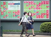  ?? (AP) ?? People walk by an electronic stock board of a securities firm in Tokyo, July 14, 2021. Asian shares were mostly lower on Wednesday, tracking a decline on Wall Street as investors weighed the latest quarterly earnings reports and inflation.