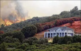  ?? MARCIO JOSE SANCHEZ / AP ?? A wildfire crests over a ridge, threatenin­g a home Monday in Lakeport, Calif. The city’s downtown became a ghost town with main streets deserted.