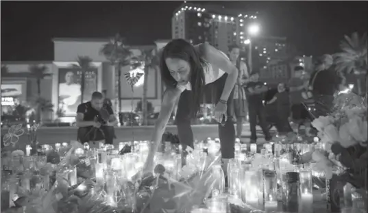  ?? DREW ANGERER, GETTY IMAGES ?? Las Vegas resident Elisabeth Apcar lights candles at a makeshift memorial for shooting victims at the northern end of the Strip. Perched in a hotel room, a gunman opened fire at concert-goers.