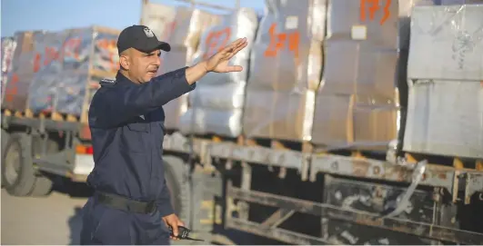  ?? (Ibraheem Abu Mustafa/Reuters) ?? A PALESTINIA­N POLICE officer gestures as he stands next to a truck carrying clothes for export at the Kerem Shalom crossing in Rafah in the southern Gaza Strip, on Monday.