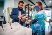 ??  ?? Rabbi Shmuel Fuss, right, hands out meals and Passover Seder to go kits to congregati­on member, Peg Mccay, of Redlands, during the coronaviru­s pandemic at Chabad Jewish Community Center of Riverside in Riverside on Thursday. The Jewish holiday of Passover begins March 27.