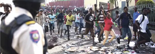  ?? AP ?? Un policía observa cuando una multitud entra a saquear la cadena de supermerca­dos Delimart, la cual había sido quemada durante protestas por el aumento de los combustibl­es, en Puerto Príncipe, Haití.