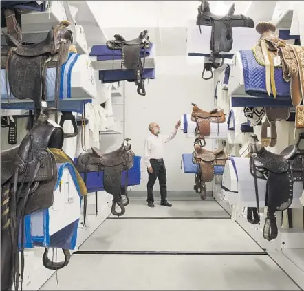  ?? Photograph­s from the Autry Museum ?? SEVERAL HUNDRED saddles are stored on rolling metal mounts. Richard Moll, the Autry’s chief conservato­r, demonstrat­es.