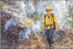  ?? Cory Rubin/ The Signal ?? A Los Angeles County Fire camp crew member walks through smoulderin­g brush behind an apartment complex on the 24400 block of Newhall Avenue.