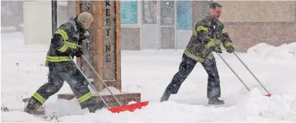  ?? —AP ?? MANDAN, North Dakota: Mandan firefighte­rs Shane Weltikol (left) and Chad Nicklos clear accumulati­ng snow from outside the firehouse in downtown Mandan as the Christmas Day blizzard intensifie­s on Sunday.