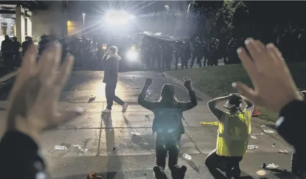  ??  ?? 0 Protesters kneeling and raising up their arms in front of a line of police officers at the Brooklyn Center Police Station during a protest