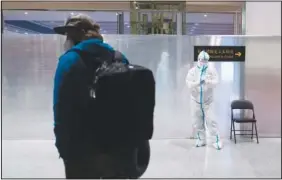  ?? ?? A passenger waits Monday in the holding area in front of a member of airport personnel wearing protective gear at the Beijing Capital Internatio­nal Airport.