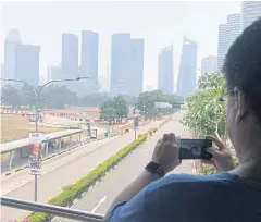  ?? AP ?? A tourist takes pictures in front of the central business district shrouded in haze in Singapore yesterday.