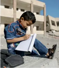  ?? AFP ?? A Yemeni boy writes as he sits outside a school, that was damaged in fighting in the southern Yemeni city of Taez.—