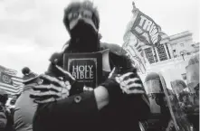  ??  ?? A man holds a Bible as Trump supporters gather outside the Capitol in Washington on Jan. 6. [JOHN MINCHILLO/THE ASSOCIATED PRESS VIA USA TODAY]