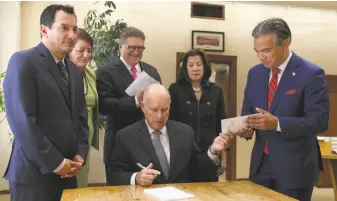  ?? Photos by Rich Pedroncell­i / Associated Press ?? Gov. Jerry Brown (seated) hands a copy of the bill to end bail after signing it to Assemblyma­n Rob Bonta, D-Alameda, co-author with state Sen. Bob Hertzberg, D-Van Nuys (third from left).