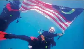  ??  ?? A diver ‘flying’ the Jalur Gemilang underwater at Tunku Abdul Rahman Park in Kota Kinabalu.