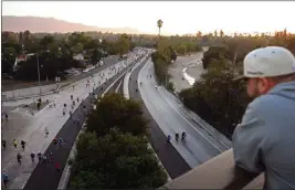  ?? PHOTO BY ANDY HOLZMAN ?? A man watches ArroyoFest participan­ts proceed along the 110Freeway on Sunday from the York Boulevard overpass. After 11a.m., the freeway reopened to drivers.