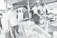  ?? ?? MESRA: Ahli Dewan Undangan Negeri (ADUN) Jepak Iskandar Turkee (kiri) yang beramah mesra dan menyerahka­n apron kepada seorang peniaga roti canai.