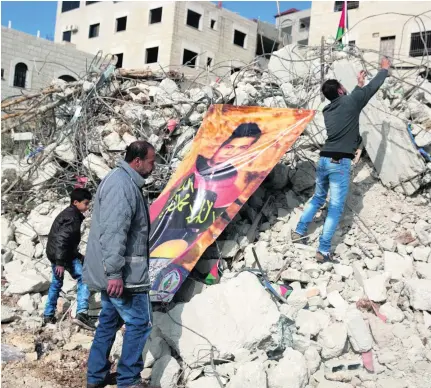  ?? Photos: Heidi Levine For The National. ?? Mohanad Halabi’s father, Shafiq stands by the rubble of his family home that was destroyed by Israel, as his sons Mustafa, 10, left, and Mohammed 21, secure a giant poster to the twisted metal showing a portrait of his late son.