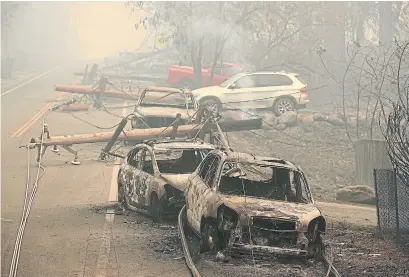  ?? JUSTIN SULLIVAN GETTY IMAGES ?? Power lines rest on torched cars in Paradise. One sheriff called the massive fires “the event that we have feared for a long time.”
