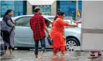  ?? — Photos by M. Sajjad ?? Pedestrian­s cross a flooded road in Al Mahatta, Sharjah, on Monday morning, while others in Al Qasmiya area help each other out as they wade in the waters with their pants rolled up and shoes taken off.