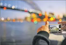  ?? Picture: REUTERS ?? A tourist takes a photograph on their iPhone of the Sydney Harbour Bridge at sunset on a spring day in central Sydney, Australia.