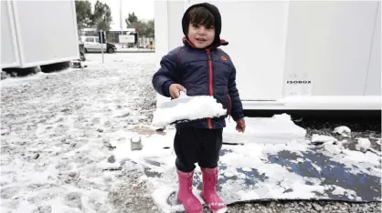  ?? —AFP ?? LESBOS: A child plays in the snow at the Kara Tepe camp on the island of Lesbos following heavy snowfalls yesterday. The number of migrants arriving in Europe by two main sea routes in 2016 plunged by almost two-thirds to 364,000 compared with the...