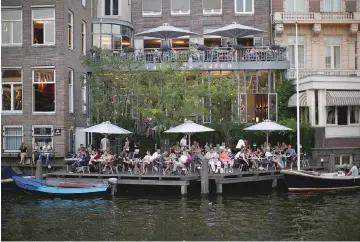  ??  ?? Customers sit at an outdoor cafe terrace on the canalside in Amsterdam.
