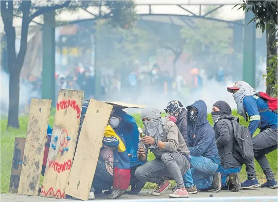  ?? AP ?? Como en una guerra. Militantes de los piquetes en Quito se parapetan detrás de unas maderas mientras preparan una bomba de combustibl­e.