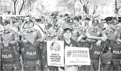  ?? — Gambar AFP ?? SOKONGAN PADU: Penyokong Sereno menunjukka­n plakad mengkritik Duterte di hadapan sekumpulan polis yang berkawal semasa perhimpuna­n di hadapan bangunan mahkamah agung di Manila, semalam.