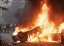  ?? Demonstrat­ors stand in front of a burning car during a protest of Yellow vests (Gilets jaunes) against rising oil prices and living costs in Paris on Saturday. ??