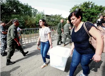  ?? AFP ?? Lebanese electoral registrars walk past policemen as they carry away a sealed electoral ballot box containing new ballots marked for the various religious sects according to Lebanese confession­al voting rules from a government office in the capital Beirut, on their way back to their polling stations on Saturday. —