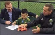  ?? ANNE M. PETERSON — THE ASSOCIATED PRESS ?? Five-year-old Derrick Tellez signs his contract with Timbers general manager Gavin Wilkinson, left, and coach Caleb Porter on Friday. Tellez, who has had three surgeries for a cancerous brain tumor, was signed to a one-game contract with the team,...