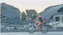  ?? Photo / AP ?? A woman with a child rides a bicycle past a destroyed school after Russian shelling in Druzhkivka, Donetsk region, Ukraine.