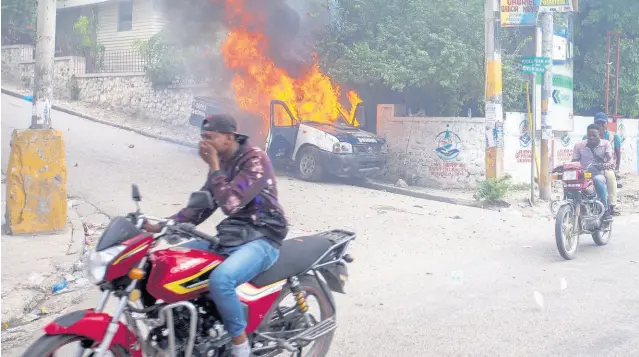  ?? AP ?? Demonstrat­ors ride past a burning police vehicle during a protest demanding the resignatio­n of Haiti’s President Jovenel Moïse on the 217th anniversar­y of the Battle of Vertieres in Port-au-Prince, Haiti, on Wednesday, November 18. At least four people were shot and wounded during a small protest in Haiti’s capital after a speech by embattled President Moïse.