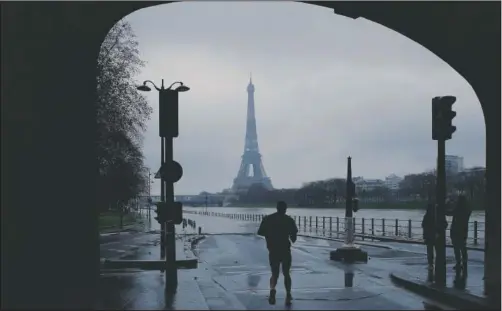  ?? (AP/Christophe Ena) ?? A man jogs near the flooded Seine River banks in Paris on Sunday.