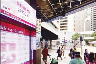  ?? (AP) ?? People wearing face masks walk in front of a bank’s electronic board showing the Hong Kong share index at Hong Kong Stock Exchange on Aug 5. Major Asian stock markets declined Wednesday amid investor concern about US
stimulus spending and a trade agreement with Beijing.